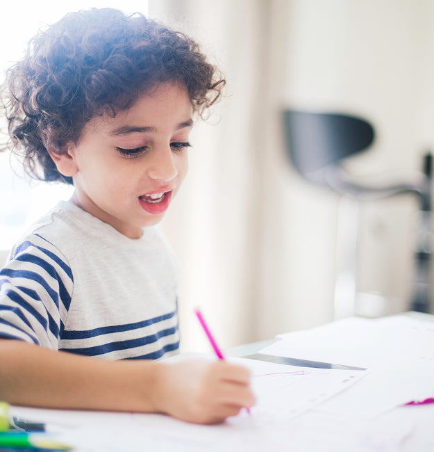 Child writing with a pink pencil at a desk
